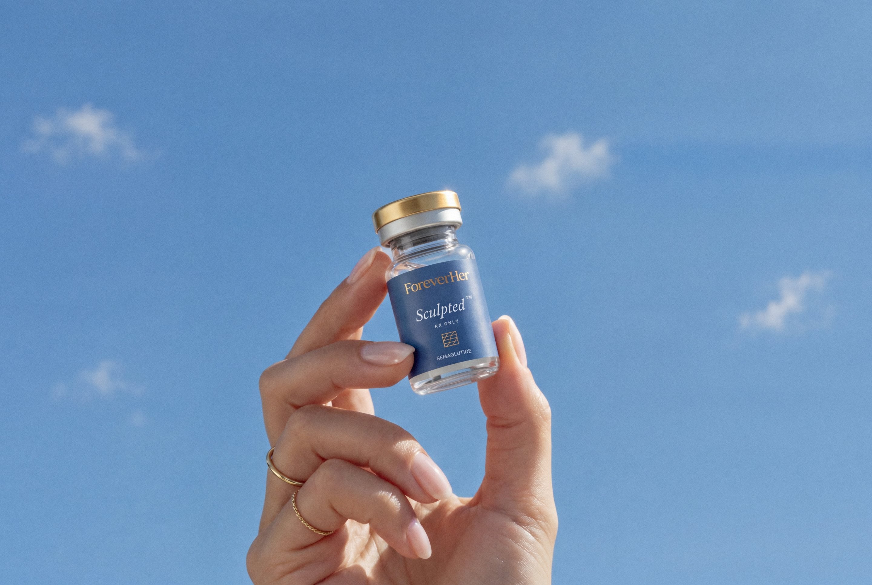 A hand holding a Sculpted vial against a blue sky